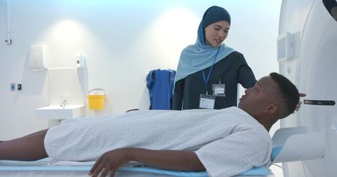 Female ct technologist in headscarf assisting african american patient on scanner