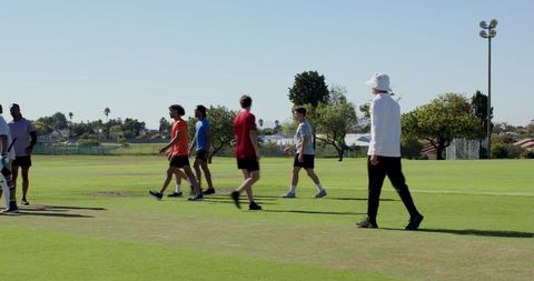 Youth athletic team walking across sunny field with coach in white bucket hat
