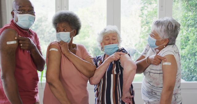 Four elderly individuals in casual clothing proudly showing their vaccine bandaids while wearing masks. Ideal for promoting vaccinations, elderly health care, COVID-19 awareness, or public health campaigns.