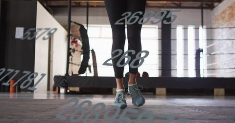 Female boxer standing on concrete gym floor with numeric overlay, backlit training scene