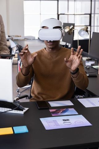 Young Professional Wearing VR Headset Gesturing at Desk in Modern Open-Plan Office