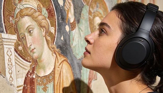 Young woman wearing headphones leaning close studying medieval fresco details in museum