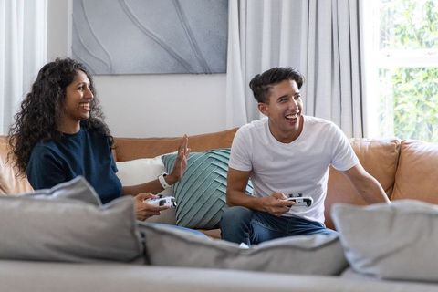 African american couple playing video games on sofa trading high five laughing at home