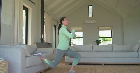 Mid-adult asian woman performing rear lunge during home workout in modern living room