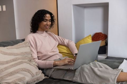 Non-binary adult reclining on cozy sofa using laptop for remote work and online learning