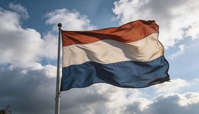 Waving dutch tricolor flag billowing on metal pole against dramatic cloudy sky with wind motion