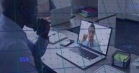 Man attending virtual meeting with data visualization overlay on laptop at shared desk