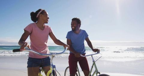 Joyful Couple Walking Bicycles on Sunlit Beach