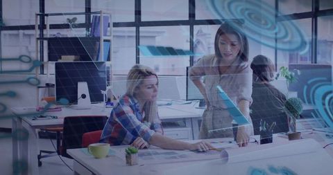 Female designers collaborating over blueprints with augmented reality overlay in open studio