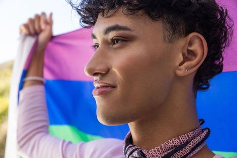 Smiling Person Holding Multicolored Pride Flag in Outdoor Setting