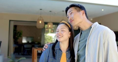Asian couple embracing on modern covered patio, leaning together in sunlit terrace