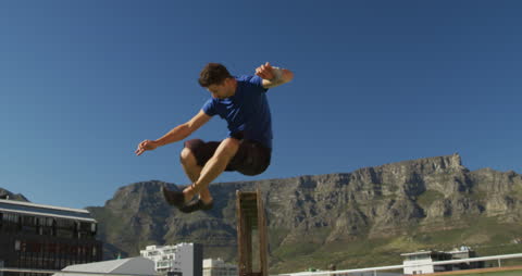 Man Practicing Parkour on Rooftop with Mountainous Cityscape