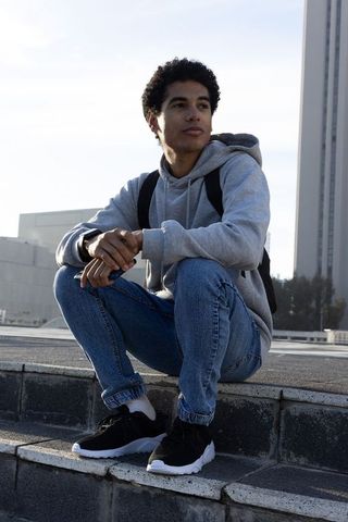 African american young man sitting on urban steps wearing hoodie and backpack