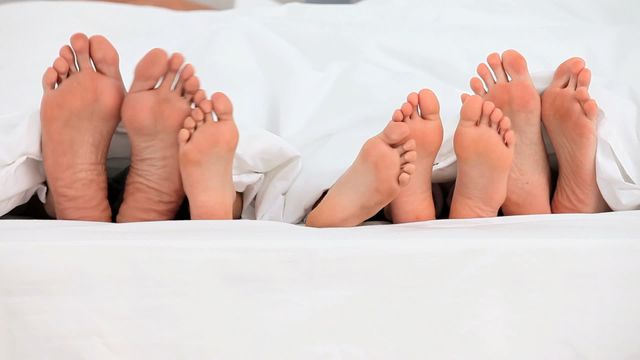 Family members' feet peeking out from under white covers, suggesting a scene of comfort and togetherness. This could be used in contexts related to family life, bedding advertisements, themes of relaxation and bonding, or articles about the importance of family connections.