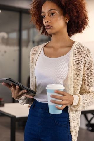 Professional woman using tablet drinking coffee modern workspace
