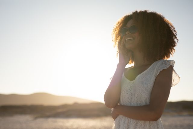 African American woman standing on a beach, wearing sunglasses, smiling, Free time and vacation. 