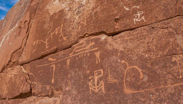 Displaying ancient petroglyph panel on red sandstone cliff in arid canyon landscape