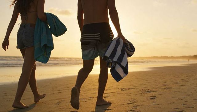Couple walking sunset beach holding towels barefoot romantic stroll