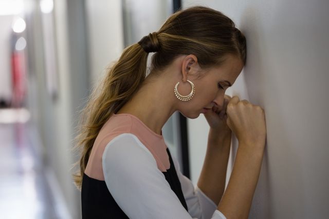 Frustrated young businesswoman leaning on wall at office