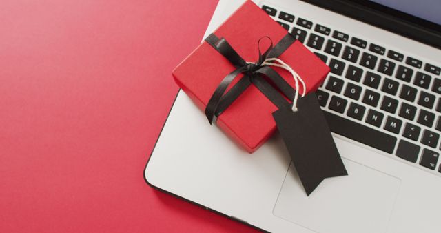 Laptop and red gift box with black ribbon and gift tag, on red background with copy space. Luxury treat, present, online shopping, black friday, sale and retail concept digitally generated image.