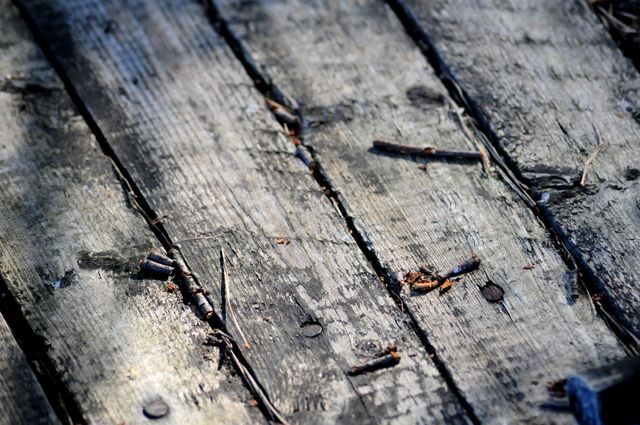Worn wooden planks showing visible signs of aging, cracks, and embedded nails. Ideal for backgrounds, textures, and design elements in rustic and vintage-themed projects. Perfect for utilizing in outdoor or historical content to evoke a sense of age and nostalgia.