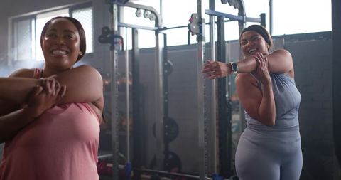 Diverse women stretching and laughing during strength training session at gym