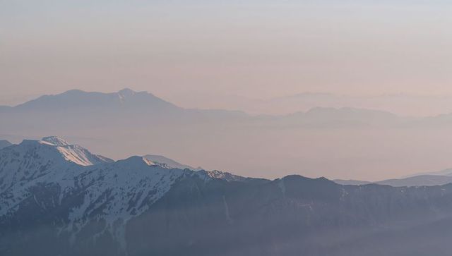 Pastel dawn over snowcapped alpine ridge with misty layered mountain horizons