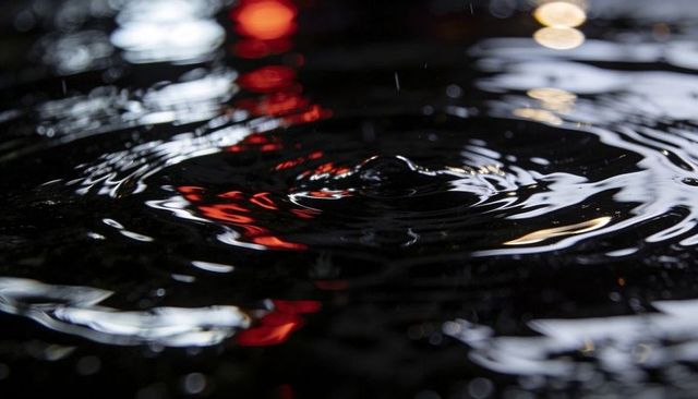 Night water surface ripples with central droplet reflecting red and white city lights