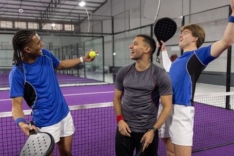 Multicultural male padel players celebrating team win on vibrant purple indoor court