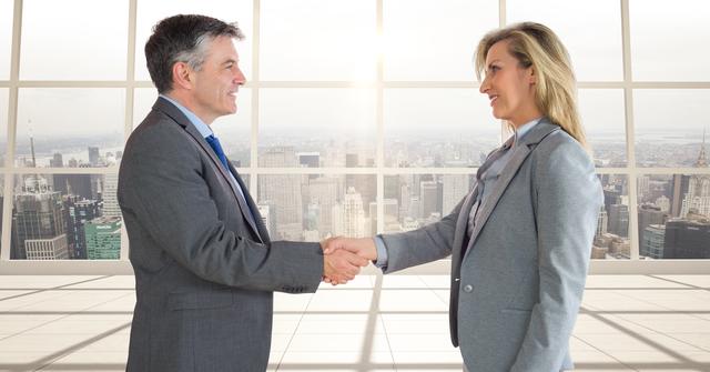 Business professionals standing in a modern office, shaking hands, signifying an agreement or partnership. Large windows offer a view of a city skyline, indicating an urban setting ideal for corporate materials or depicting teamwork, collaboration, and successful negotiations. Suitable for articles on business deals, corporate collaboration, teamwork, and leadership.