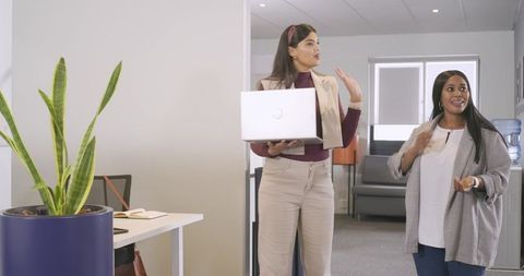 Diverse coworkers collaborating in modern office reception holding laptop and chatting