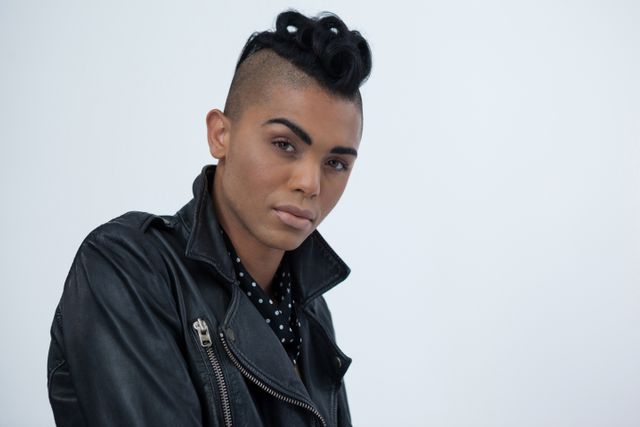 Transgender woman standing confidently against a white background, wearing a leather jacket and polka dot shirt. Ideal for use in articles, blogs, and campaigns focused on gender identity, LGBTQ rights, fashion, and self-expression.
