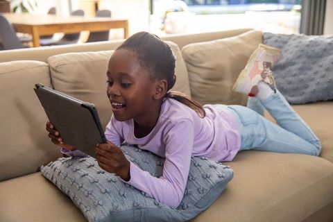 African american girl lying on sofa using tablet for learning, playing and relaxing