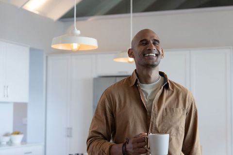 African american man smiling in modern kitchen holding white ribbed mug, relaxed morning