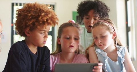 Elementary Students Leaning Around Tablet Collaborating and Learning Together
