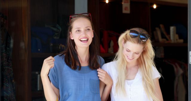 Two young women are smiling and laughing outdoors, enjoying each other's company. They are casually dressed, indicating a relaxed and friendly atmosphere. This image is perfect for conveying concepts of friendship, joy, happiness, togetherness, and casual social interaction. It can be used in advertising, social media, blog posts, and lifestyle magazines.