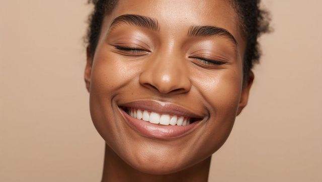 Closeup smiling young woman with glowing skin and closed eyes conveying joyful beauty