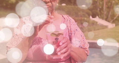 Senior woman sipping refreshing mint cocktail poolside in patterned cover-up sunlit bokeh