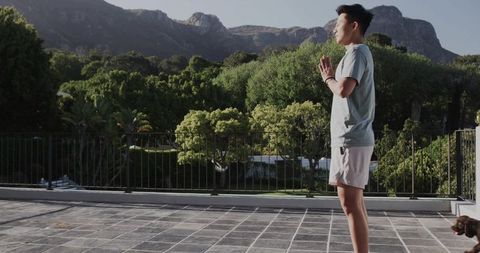 Asian man practicing meditation on tiled terrace with mountain view and wristwatch