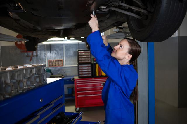 Beautiful female mechanic examining car at repair garage