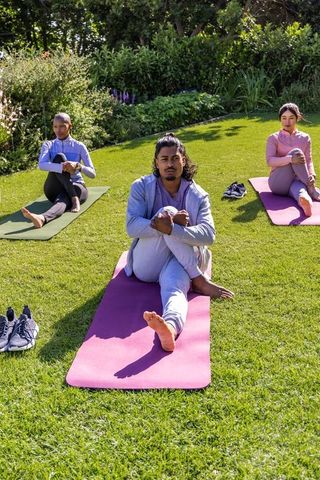 African american man and diverse classmates practicing seated knee-hold yoga outdoors on colorful ma