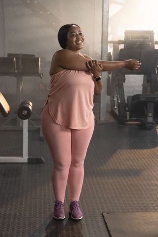Confident african american woman stretching arm in gym wearing pink activewear