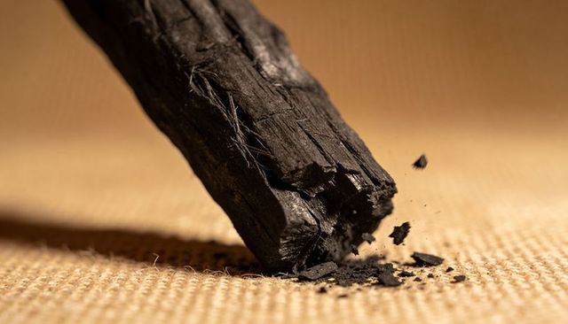 Cracked charcoal log shedding splinters on woven burlap macro texture in warm light