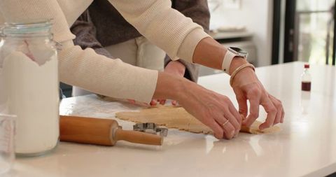 Two women rolling and cutting cookie dough on glossy modern kitchen island baking together