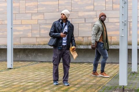 Diverse young men standing and walking in urban plaza holding smartphone and takeaway bag