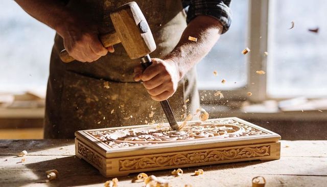 Master Woodworker Carving Ornate Relief Panel with Mallet and Chisel in Sunlit Workshop