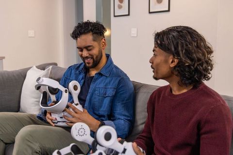 Indian friends tinkering and assembling white robot head on sofa, hobbyist makers at home