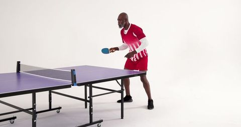 Senior Man Engaging in Competitive Ping-Pong on Purple Table