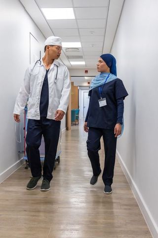 Walking and talking healthcare team in corridor, nurse wearing headscarf and doctor
