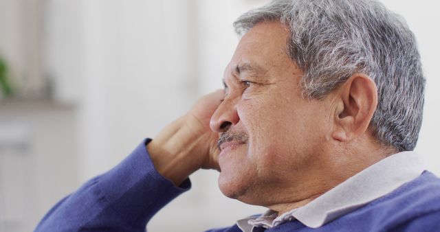 Senior man with grey hair and mustache wearing a blue sweater relaxing comfortably indoors. This image is perfect for depicting peaceful moments, retirement lifestyle, senior health, and personal contemplation.